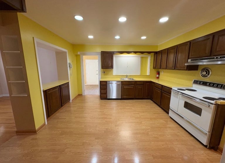 Modern kitchen with bright yellow walls, dark wood cabinets, stainless steel appliances, and hardwood flooring