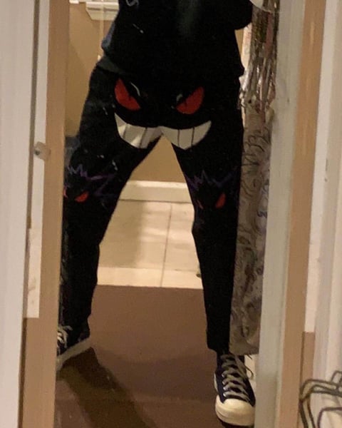 Person wearing black cat costume with red glowing eyes and buck teeth, standing in hallway