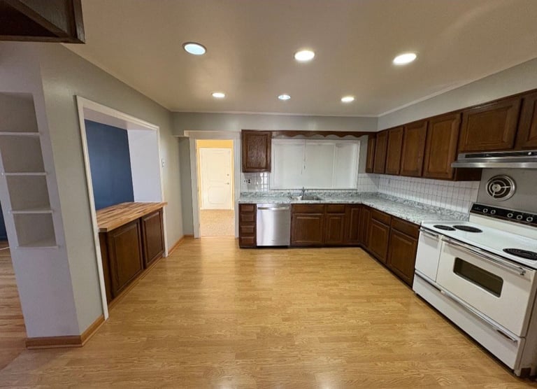 Spacious kitchen with wood cabinets, white appliances, tile backsplash, and laminate flooring with open layout.