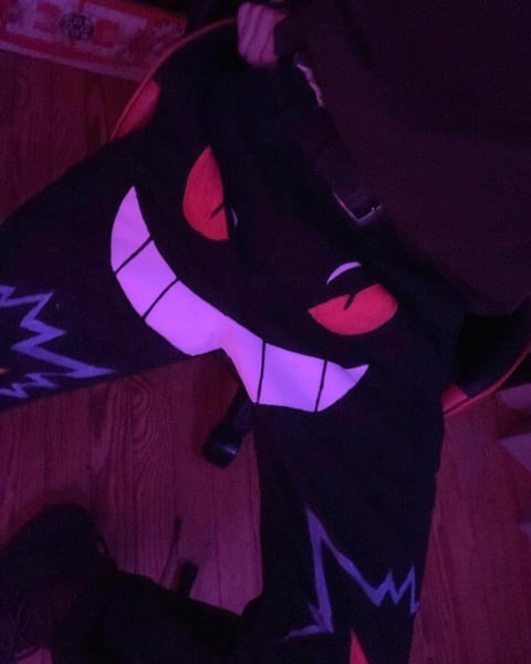 Cartoon character with black silhouette, glowing neon pink and purple features including large smile and eyes against dark background