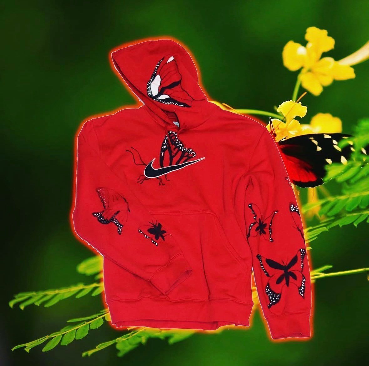 Red hoodie with black spider designs on green background with yellow flowers