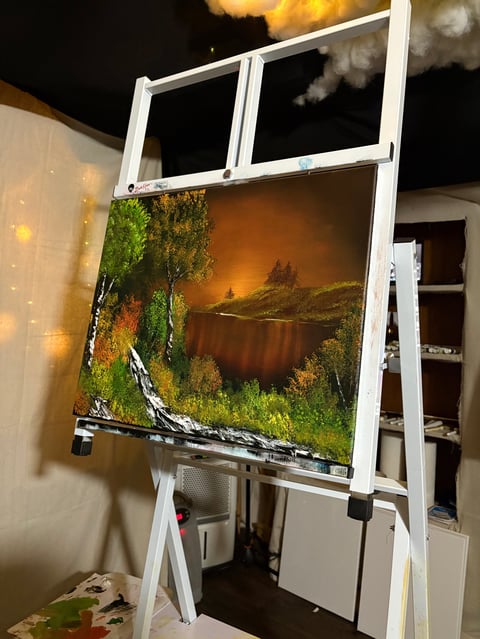 Landscape painting displayed on white wooden easel in home interior with warm lighting