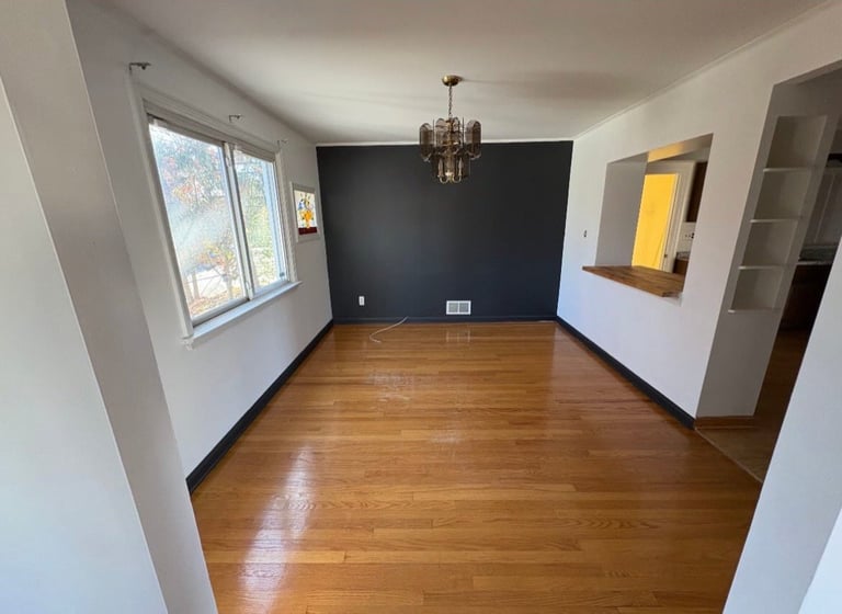 Empty living room with wood floors, white walls, dark blue accent wall, and hanging pendant light fixture
