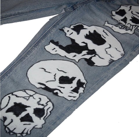 Distressed blue jeans with black and white skull graphic prints down the leg