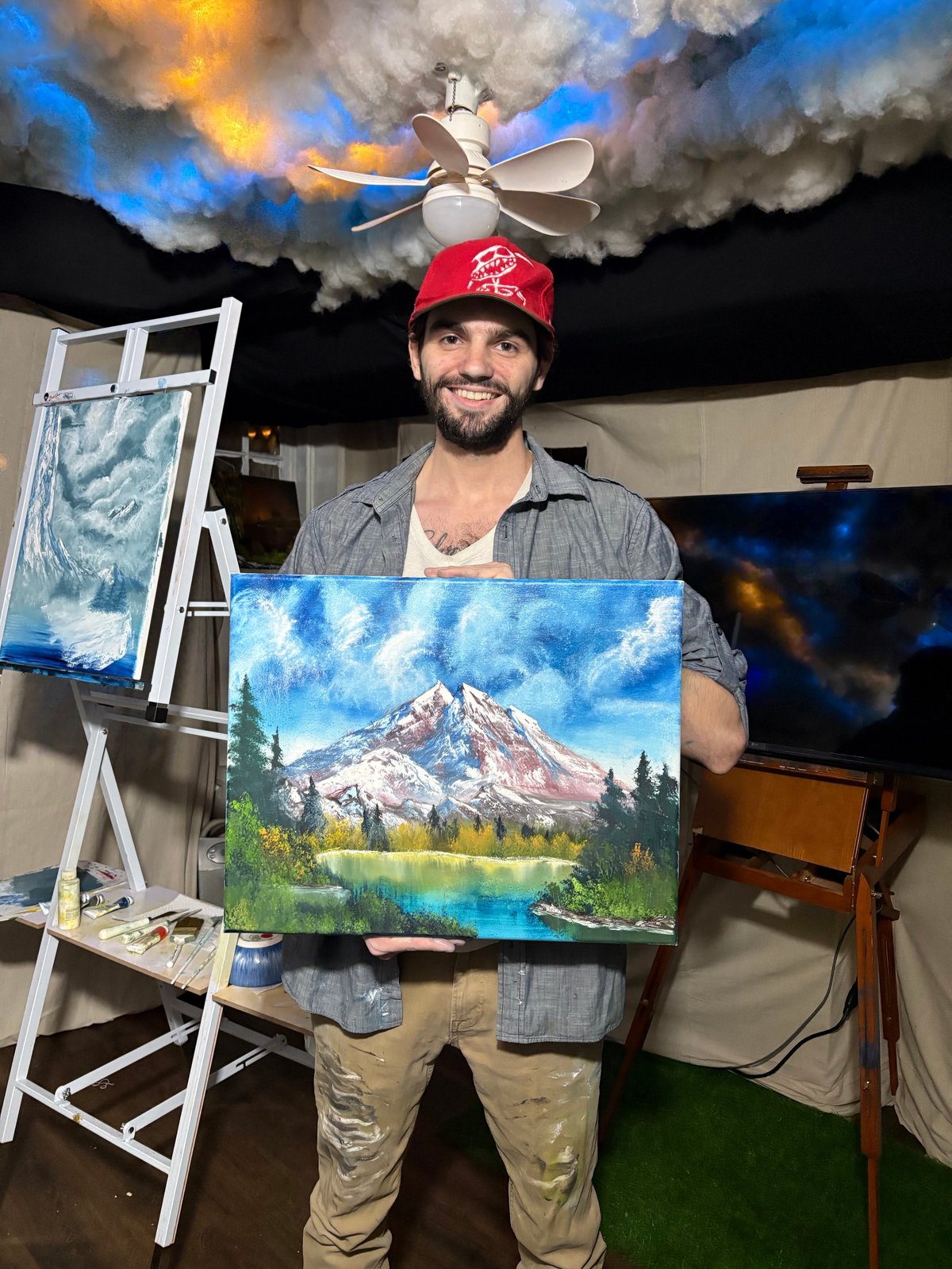 Artist Terrance Darragh holding mountain landscape painting in studio