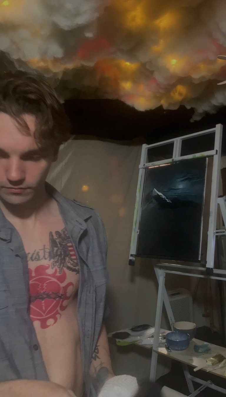 Person with tattoo standing indoors with dramatic stormy sky mural on wall and window behind them