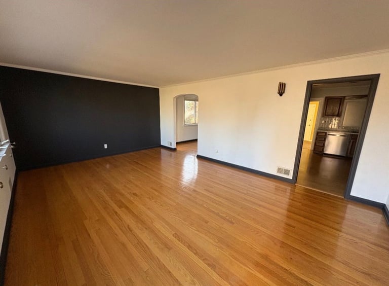 Empty living room with wooden floor, black accent wall, white walls, and doorways leading to other areas