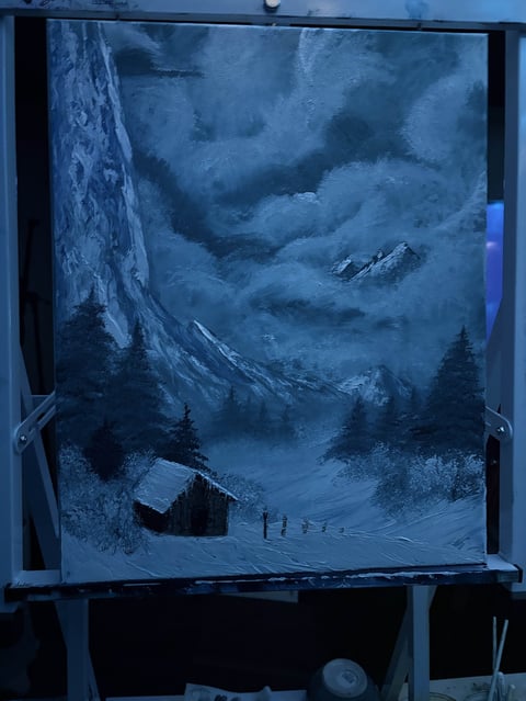 Snowy mountain landscape with cabin and figures below towering peaks displayed on a dark framed screen